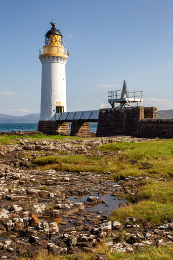 View of Tobermory Lighthouse with its white tower and yellow lantern room standing on a rocky coastline under a clear blue sky Isle of Mull Scotland United Kingdom. View of Tobermory Lighthouse with its white tower and yellow lantern room standing on a rocky coastline under a clear blue sky Isle of Mull Scotland United Kingdom.
