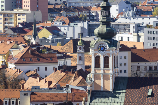 View of terracotta rooftops cascading around a clock tower a tapestry of ochre and cream buildings basking in the light framed by the city skyline Graz Styria Austria. View of terracotta rooftops cascading around a clock tower a tapestry of ochre and cream buildings basking in the light framed by the city skyline Graz Styria Austria.
