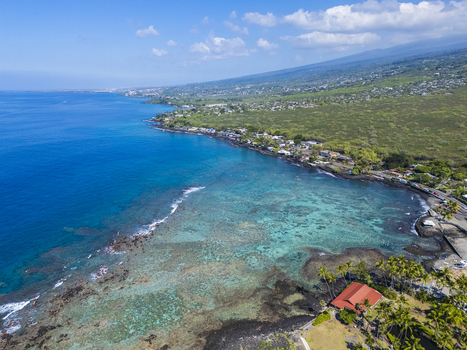 Aerial view of Kahalu u Beach Park featuring the vibrant turquoise coral reef black lava rock coastline and lush palm trees in Kailua Kona Hawaii United States. Aerial view of Kahalu u Beach Park featuring the vibrant turquoise coral reef black lava rock coastline and lush palm trees in Kailua Kona Hawaii United States.
