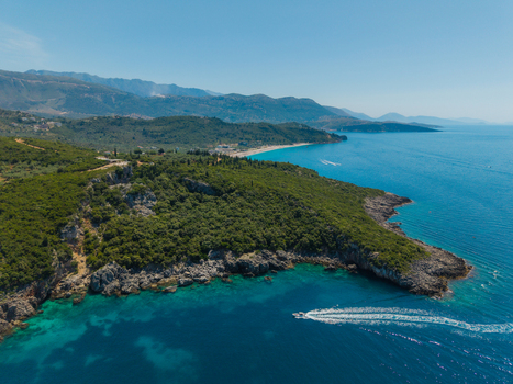 Aerial view of Aquarium Beach featuring crystal clear turquoise waters rugged rocky cliffs and dense green vegetation under a clear blue sky Jala Vlore County Albania. Aerial view of Aquarium Beach featuring crystal clear turquoise waters rugged rocky cliffs and dense green vegetation under a clear blue sky Jala Vlore County Albania.