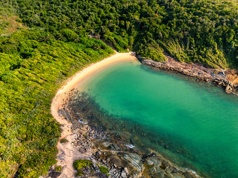 Aerial view of Praia do Ermitao featuring a secluded sandy beach with turquoise waters surrounded by lush green Atlantic forest and rocky coastline in Guarapari Espirito Santo Brazil. Aerial view of Praia do Ermitao featuring a secluded sandy beach with turquoise waters surrounded by lush green Atlantic forest and rocky coastline in Guarapari Espirito Santo Brazil.