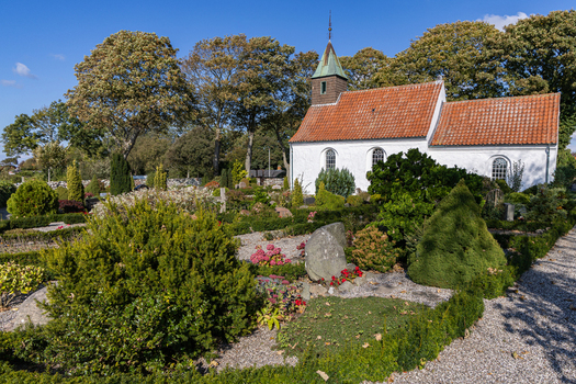 View of Hjarno Church with white walls and red tiled roof surrounded by a cemetery with lush green shrubs and manicured hedges in Hjarno Hedensted Municipality Denmark. View of Hjarno Church with white walls and red tiled roof surrounded by a cemetery with lush green shrubs and manicured hedges in Hjarno Hedensted Municipality Denmark.