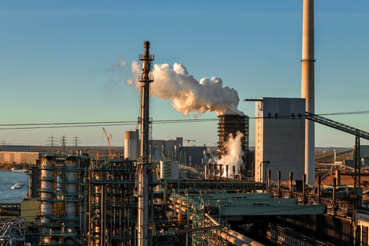 View of an industrial steel plant with smoking chimneys and complex piping systems under a clear sky during sunset Duisburg North Rhine Westphalia Germany.