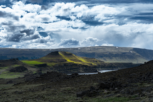 View of Hvalfjordur fjord with sunlight illuminating a green volcanic hill under a dramatic cloudy sky in Iceland. View of Hvalfjordur fjord with sunlight illuminating a green volcanic hill under a dramatic cloudy sky in Iceland.