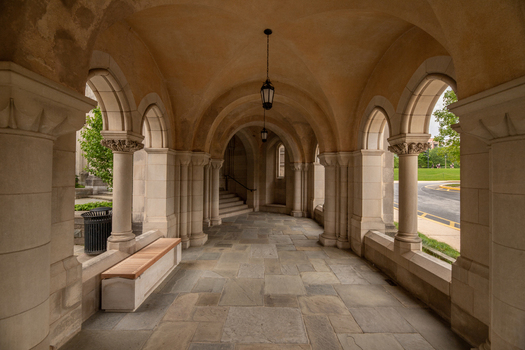 Washington United States 06 May 2025 View of Washington National Cathedral featuring a stone arched walkway with vaulted ceilings hanging lanterns and a wooden bench.