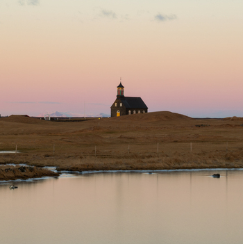 Aerial view of Hvalsneskirkja church set in a vast barren landscape with a calm pond in the foreground under a soft sunset sky in Sudurnesjabaer Iceland. Aerial view of Hvalsneskirkja church set in a vast barren landscape with a calm pond in the foreground under a soft sunset sky in Sudurnesjabaer Iceland.