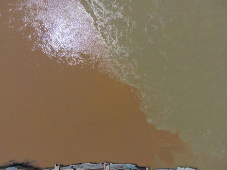 Aerial view of the confluence of the Zanskar and Indus rivers showing two distinct water colors meeting along a rocky riverbank with people visible in Ladakh Division Ladakh India. Aerial view of the confluence of the Zanskar and Indus rivers showing two distinct water colors meeting along a rocky riverbank with people visible in Ladakh Division Ladakh India.