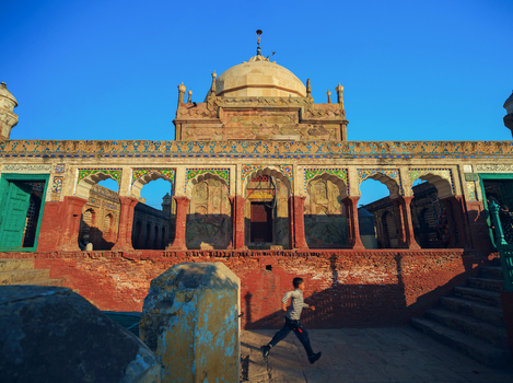 View of the historic Tomb of Shah Burhan with a young boy running past the intricate arches and decorative masonry in Chiniot Punjab Pakistan.