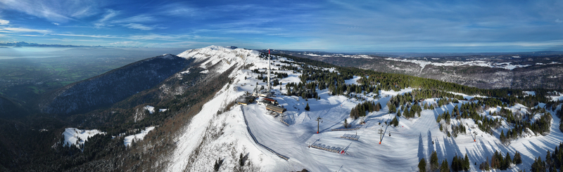 Aerial view of snow covered slopes and dark green forests meet under a vast blue sky at the ski resort Gex Auvergne Rhône Alpes France. Aerial view of snow covered slopes and dark green forests meet under a vast blue sky at the ski resort Gex Auvergne Rhône Alpes France.