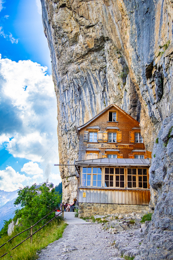 View of a rustic wooden building clings precariously to a sheer cliff face nestled beneath a dramatic overhang in Schwende Rüte Appenzell Innerrhoden Switzerland. View of a rustic wooden building clings precariously to a sheer cliff face nestled beneath a dramatic overhang in Schwende Rüte Appenzell Innerrhoden Switzerland.