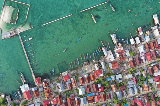 Aerial view of Pulau Maginti featuring a coastal village with traditional houses a long wooden pier and fishing boats in the turquoise waters of Maginti South East Sulawesi Indonesia.