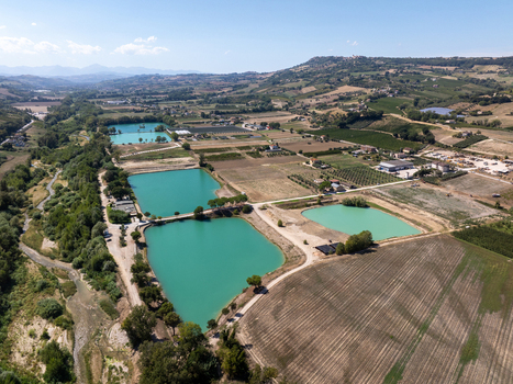 Aerial view of Laghi Santarelli featuring turquoise fishing lakes surrounded by agricultural fields vineyards and rolling hills in the countryside of Moresco Marche Italy.