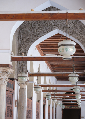 View of the Al Azhar Mosque featuring intricate stucco carvings hanging lanterns and marble columns in Cairo Egypt. View of the Al Azhar Mosque featuring intricate stucco carvings hanging lanterns and marble columns in Cairo Egypt.