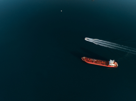 Aerial view of a large red tanker ship and a small motorboat leaving a white wake on the calm dark blue sea Augusta Sicily Italy. Aerial view of a large red tanker ship and a small motorboat leaving a white wake on the calm dark blue sea Augusta Sicily Italy.