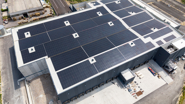 Aerial view of a modern logistics warehouse for fresh fruit and vegetable distribution featuring extensive rooftop solar panels ventilation units and loading docks in Melegnano Lombardy Italy.