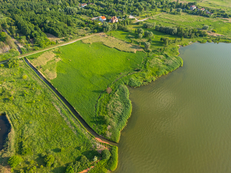 Aerial view of the Vistula Lagoon shoreline featuring lush green fields dense forest patches and a small canal flowing into the water in Tolkmicko Warmian Masurian Voivodeship Poland. Aerial view of the Vistula Lagoon shoreline featuring lush green fields dense forest patches and a small canal flowing into the water in Tolkmicko Warmian Masurian Voivodeship Poland.