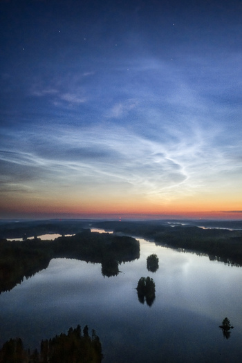 Aerial view of noctilucent clouds glowing in the twilight sky above the reflective waters and forested islands of Laaminki in Kangasniemi Etela Savo Finland.