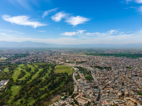 Aerial view of the historic Bala Hisar Fort surrounded by dense urban landscape green golf course winding roads and distant mountains Peshawar Khyber Pakhtunkhwa Pakistan.