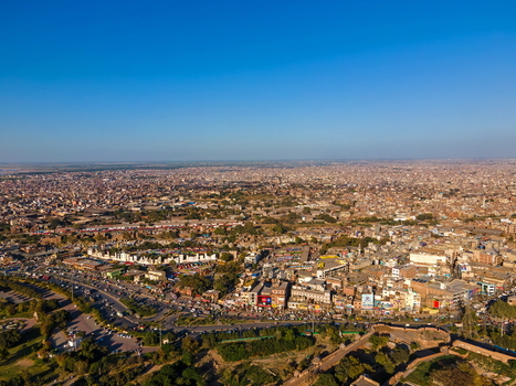Aerial view of Minar e Pakistan and the surrounding urban landscape with dense city buildings roads and greenery under a clear blue sky in Lahore Punjab Pakistan.