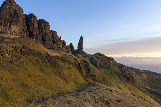 Aerial view of The Storr rocky pinnacle and dramatic cliffs overlooking grassy slopes under a soft golden sky Isle of Skye Scotland United Kingdom. Aerial view of The Storr rocky pinnacle and dramatic cliffs overlooking grassy slopes under a soft golden sky Isle of Skye Scotland United Kingdom.