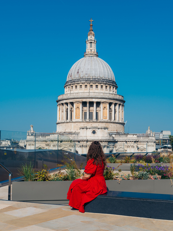 View of a woman in a flowing crimson dress admiring the majestic weathered dome of St. Paul s Cathedral under a brilliant blue sky London England United Kingdom. View of a woman in a flowing crimson dress admiring the majestic weathered dome of St. Paul s Cathedral under a brilliant blue sky London England United Kingdom.