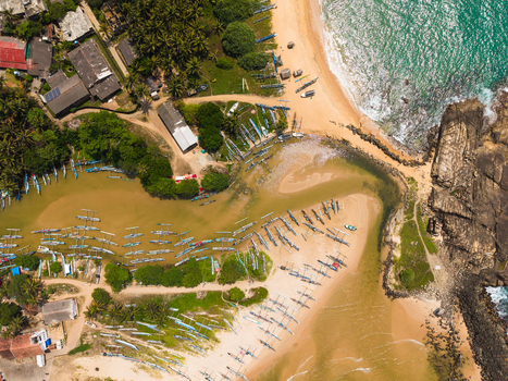 Aerial view of traditional outrigger fishing boats lined up on the sandy beach and lagoon surrounded by palm trees and coastal buildings in Dodanduwa Southern Province Sri Lanka. Aerial view of traditional outrigger fishing boats lined up on the sandy beach and lagoon surrounded by palm trees and coastal buildings in Dodanduwa Southern Province Sri Lanka.