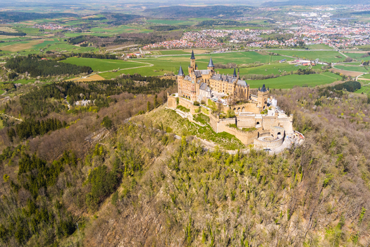 Burg Hohenzollern Baden Wurttemberg Germany 27 September 2026 Aerial view of Hohenzollern Castle perched on a forested hilltop surrounded by lush green fields and rolling landscapes.