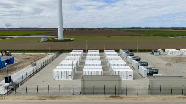 Aerial view of a battery energy storage system with rows of white containers on a paved industrial site near a wind turbine in Dronten Flevoland Netherlands.