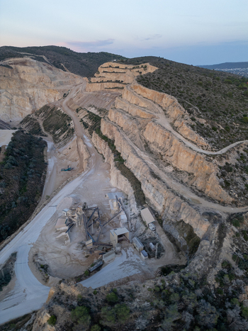 Aerial view of an open pit stone quarry with terraced rock walls heavy machinery and processing facilities in the hilly landscape of Teulada Valencian Community Spain.