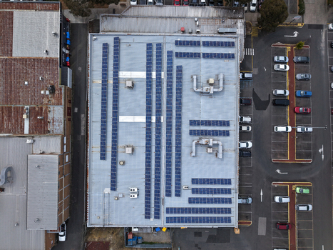 Melbourne VIC Australia 25 September 2026 Aerial view of a factory roof covered with rows of solar panels adjacent to a parking lot with various cars.