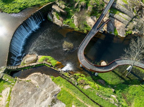 Aerial view of Acude da Ribeira with its curved dam and modern pedestrian bridge over the river surrounded by rocky banks and lush greenery in Ervedal Coimbra Portugal. Aerial view of Acude da Ribeira with its curved dam and modern pedestrian bridge over the river surrounded by rocky banks and lush greenery in Ervedal Coimbra Portugal.