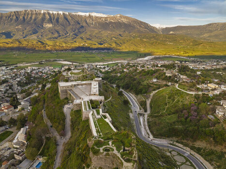 Aerial view of Gjirokaster Fortress perched on a hill with historic stone walls surrounded by the town and scenic mountains in Gjirokaster Gjirokaster County Albania. Aerial view of Gjirokaster Fortress perched on a hill with historic stone walls surrounded by the town and scenic mountains in Gjirokaster Gjirokaster County Albania.