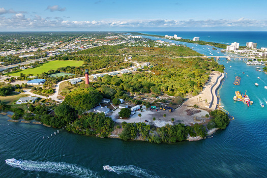 Aerial view of the Jupiter Inlet Lighthouse standing tall amidst lush greenery and sparkling waterways a coastal beacon under a vast blue sky Jupiter Florida United States.