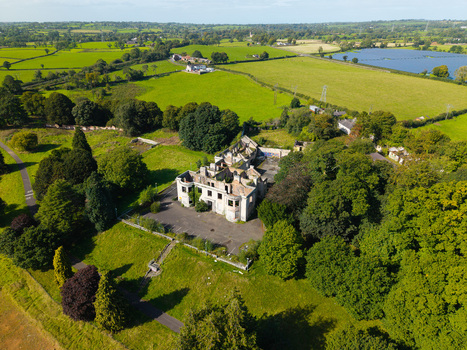 Aerial view of a ruined mansion surrounded by lush green fields dense trees and a nearby lake in Lisburn Northern Ireland United Kingdom. Aerial view of a ruined mansion surrounded by lush green fields dense trees and a nearby lake in Lisburn Northern Ireland United Kingdom.