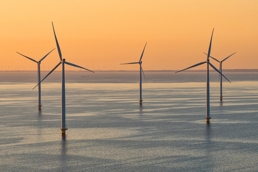 Aerial view of an offshore wind farm with several wind turbines standing in calm sea water under a golden sunset sky Netherlands.