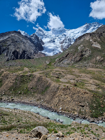 View of the Penzi La road winding through the rugged mountain landscape with a glacier and snow capped peaks above a river in Zanskar Ladakh India.