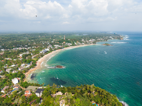 Aerial view of the turquoise waters and sandy shoreline of Mirissa Beach surrounded by lush tropical greenery and coastal buildings in Mirissa Southern Province Sri Lanka. Aerial view of the turquoise waters and sandy shoreline of Mirissa Beach surrounded by lush tropical greenery and coastal buildings in Mirissa Southern Province Sri Lanka.