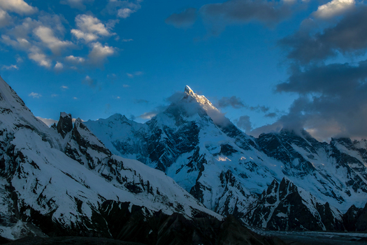 View of the snow covered peak of Masherbrum mountain under a blue sky with scattered clouds at sunset Skardu Gilgit Pakistan. View of the snow covered peak of Masherbrum mountain under a blue sky with scattered clouds at sunset Skardu Gilgit Pakistan.