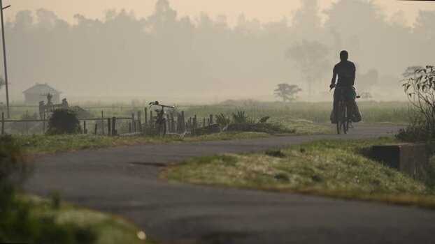 View of a cyclist on a misty rural road in Bogura Bangladesh.