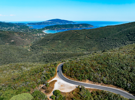 Aerial view of the winding road at Passo del Monumento surrounded by lush Mediterranean vegetation and hills overlooking the blue sea in Campo nell Elba Toscana Italy.