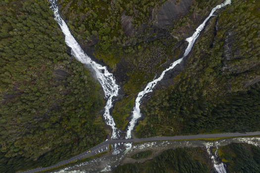 Aerial view of the twin Latefossen waterfall cascading through dense pine forests and under a stone bridge in Skare Vestland Norway.