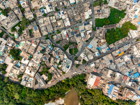 Aerial view of the dense urban fabric with traditional flat roofed buildings narrow winding streets and lush green trees bordering a water body Udaipur Rajasthan India. Aerial view of the dense urban fabric with traditional flat roofed buildings narrow winding streets and lush green trees bordering a water body Udaipur Rajasthan India.