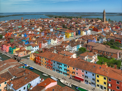 Aerial view of vibrant multicolored houses lining narrow canals with the iconic leaning tower silhouetted against the horizon Burano Venice Veneto Italy. Aerial view of vibrant multicolored houses lining narrow canals with the iconic leaning tower silhouetted against the horizon Burano Venice Veneto Italy.
