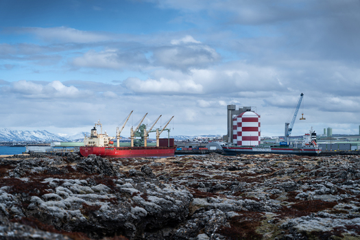 Hafnarfjordur Iceland 17 April 2026 View of a large red cargo ship docked at the port with industrial silos and snow capped mountains under a cloudy sky.