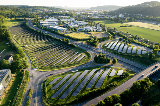 Aerial view of solar panels arranged in rows along a highway interchange surrounded by green fields and industrial buildings in Tubingen Baden Wurttemberg Germany. Aerial view of solar panels arranged in rows along a highway interchange surrounded by green fields and industrial buildings in Tubingen Baden Wurttemberg Germany.