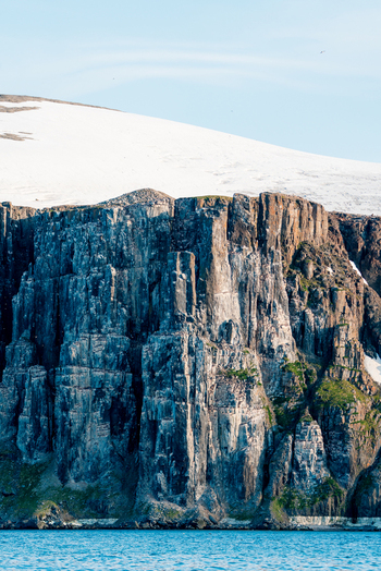 Svalbard Svalbard and Jan Mayen 22 July 2025 View of the towering basalt cliffs of Alkefjellet with a snow covered plateau and nesting seabirds above the blue water.