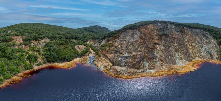 Aerial view of Laghetto delle conche a striking iron rich red lake surrounded by rocky cliffs and lush Mediterranean vegetation in Rio Marina Toscana Italy.