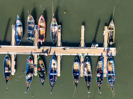 Aerial view of vibrant boats nestled against a concrete pier their reflections shimmering on the dark water Porta de Abrigo da Torreira Aveiro Portugal. Aerial view of vibrant boats nestled against a concrete pier their reflections shimmering on the dark water Porta de Abrigo da Torreira Aveiro Portugal.