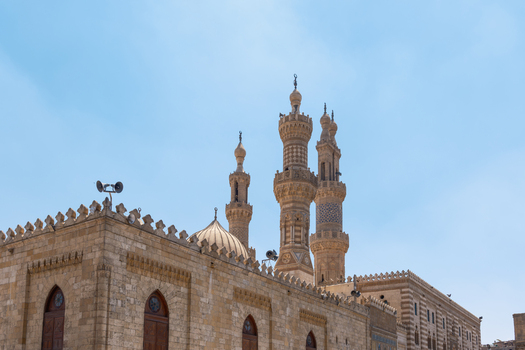 View of Al Azhar Mosque featuring its ornate stone minarets and central dome under a clear blue sky in El Darb El Ahmar Cairo Governorate Egypt. View of Al Azhar Mosque featuring its ornate stone minarets and central dome under a clear blue sky in El Darb El Ahmar Cairo Governorate Egypt.
