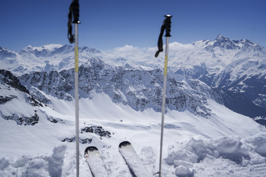 Aerial view of the snow covered Alpine peaks at La Rosiere ski resort with ski tips and poles in the foreground under a clear blue sky in Montvalezan Auvergne Rhone Alpes France.